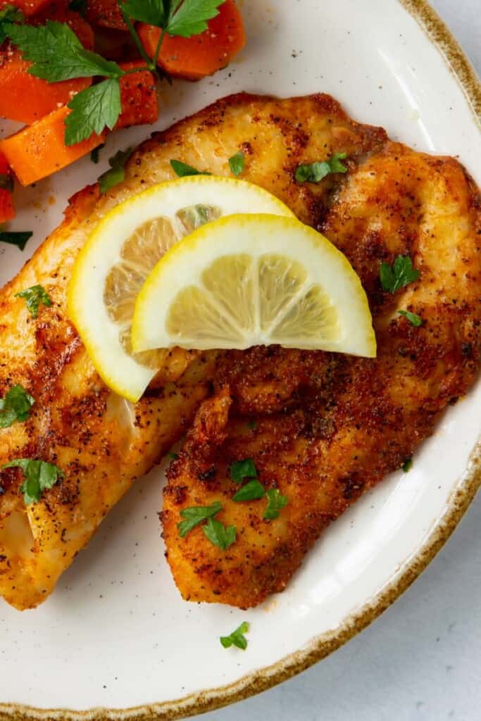 Air Fryer Tilapia on a plate with lemon wedges on top