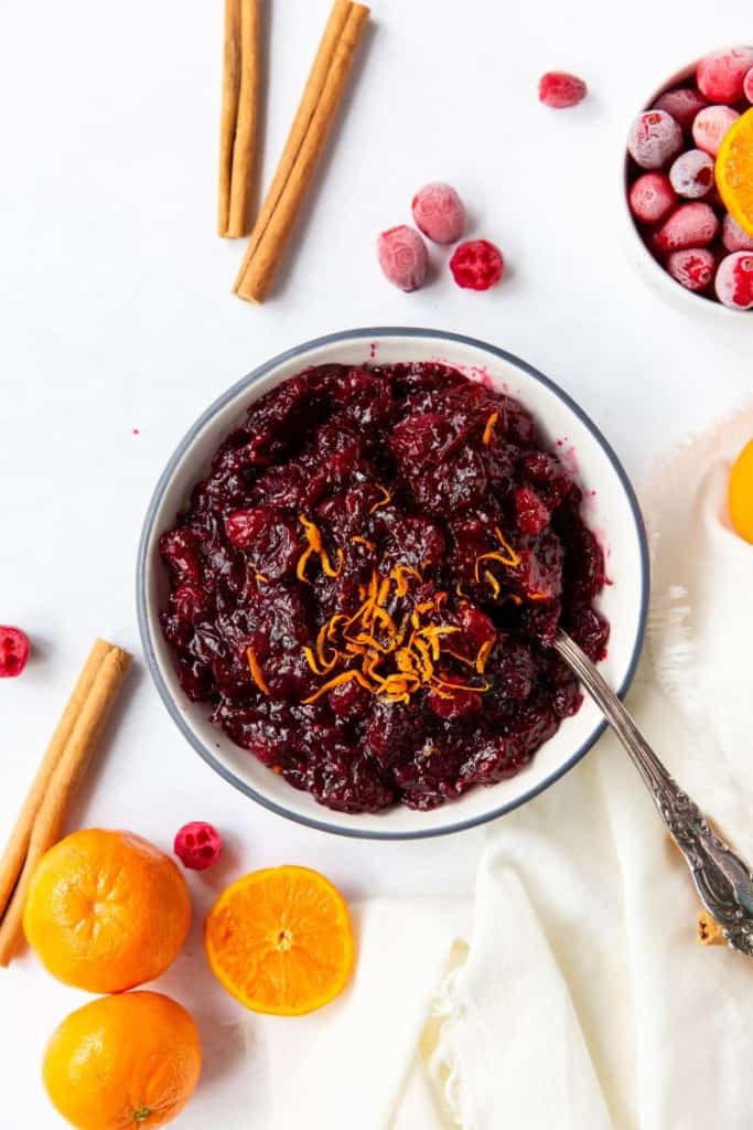 cranberry orange sauce in a bowl with a spoon with cinnamon sticks and oranges around it