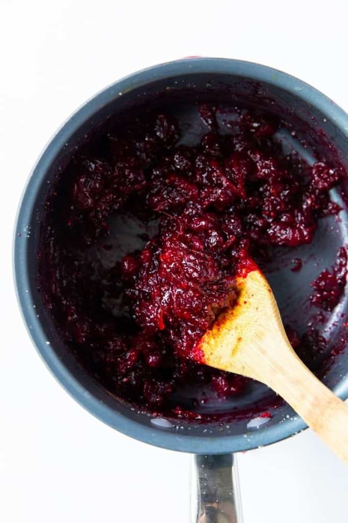 Cooked cranberry orange sauce in a saucepan with a wooden spoon in it
