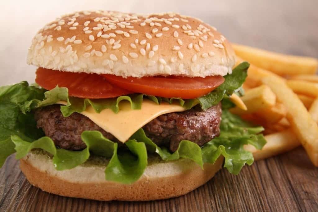 Cheeseburger on a sesame bun with lettuce and tomato on it with french fries in the background