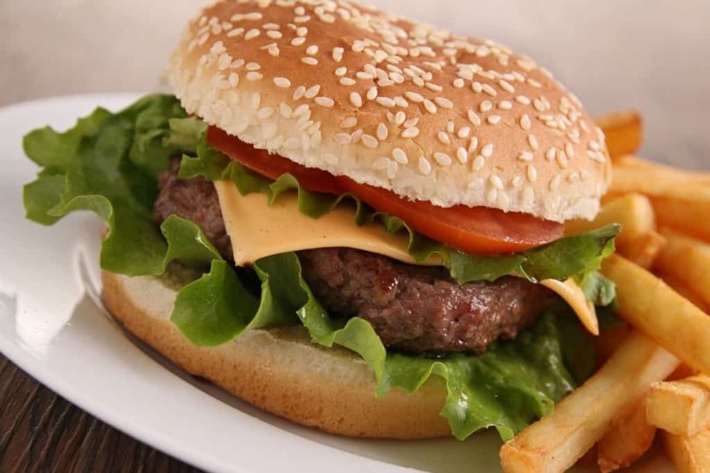 Hamburger on a sesame bun with cheese, lettuce, and tomato next to french fries