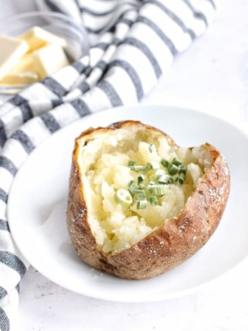 Ninja Foodi Baked Potatoes cut open topped with chives on a white plate