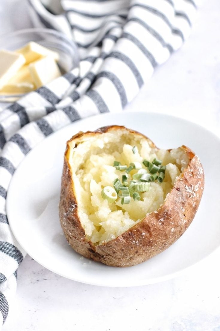 Ninja Foodi Baked Potatoes cut open topped with chives on a white plate