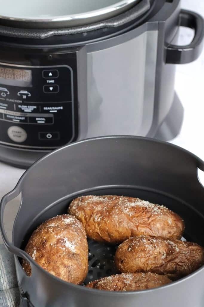 Cooked baked potatoes in pan in front of a Ninja Foodi