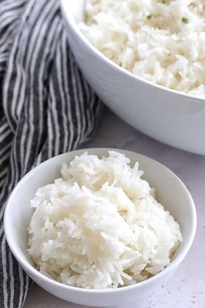 Ninja Foodi Rice in a small white bowl with a large serving bowl with rice in the corner