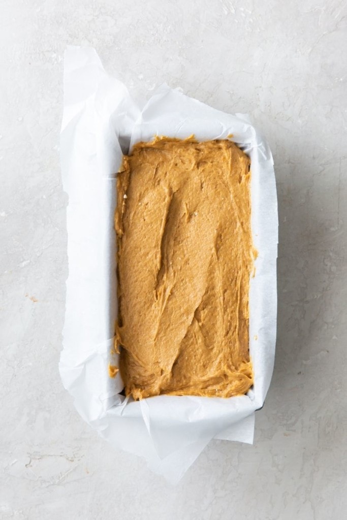 Raw pumpkin bread in a loaf pan with parchment paper around it
