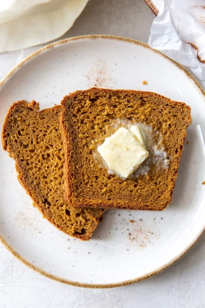 Two slices of pumpkin bread with cake mix on a white plate with a dollop of butter on one slice