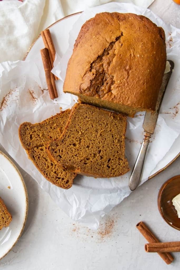 Cooked 5 ingredient pumpkin bread with 2 slices in front on a parchment paper