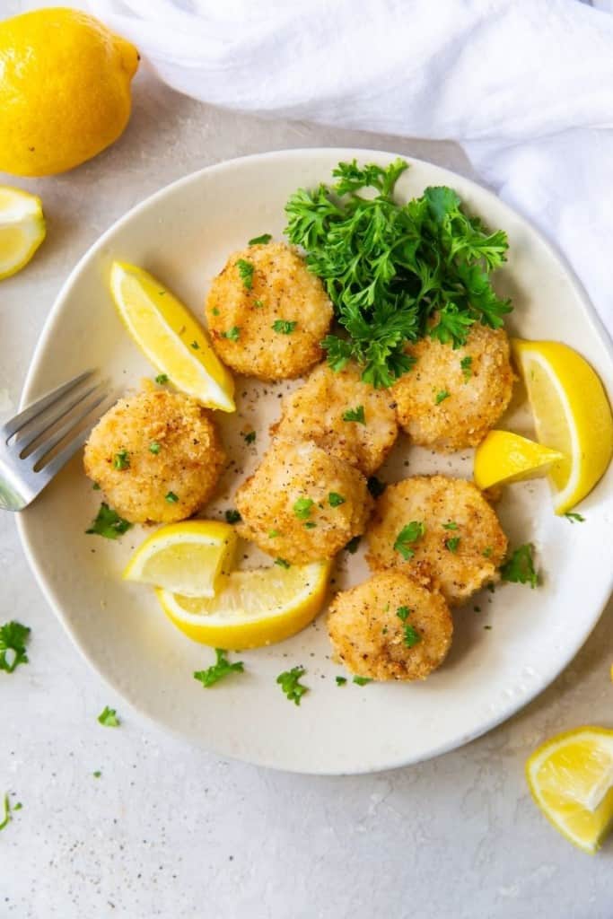 Overhead shot of air fried scallops on a plate served with lemon slices and parsley