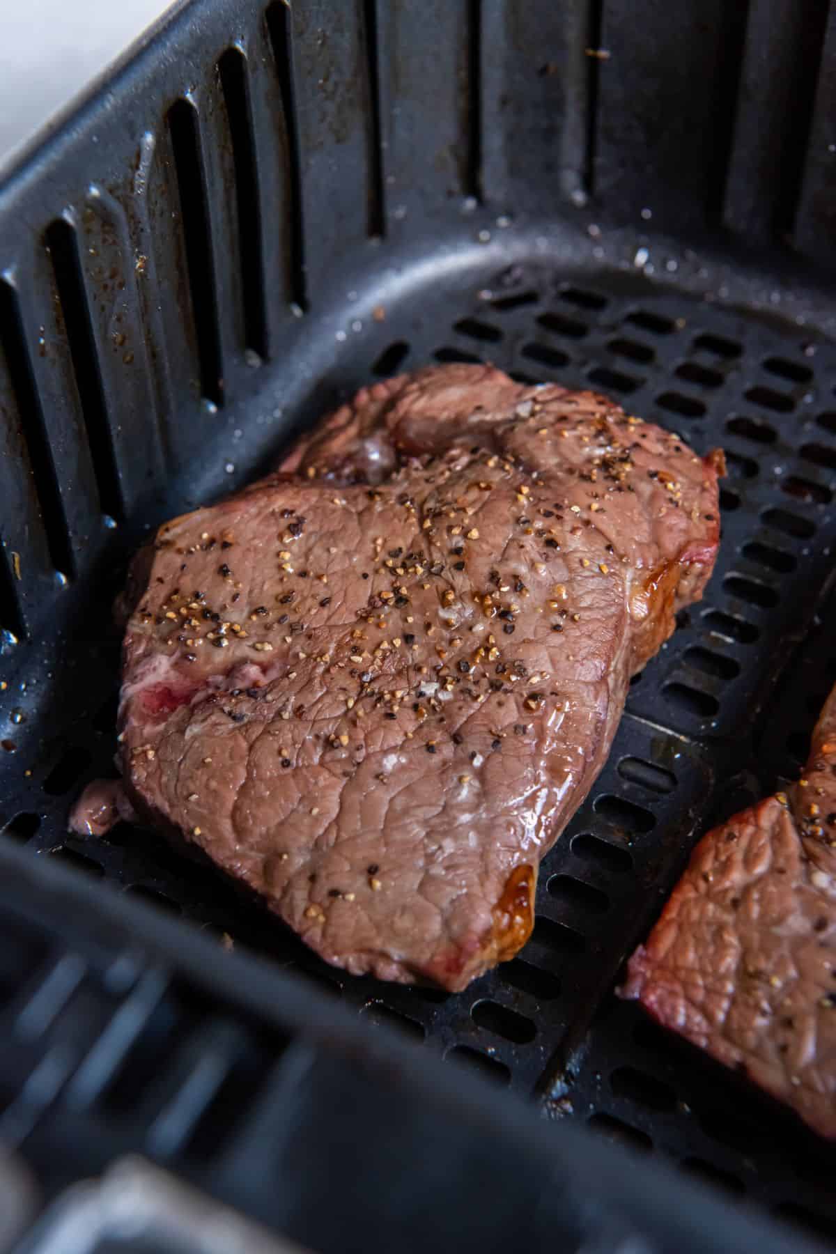 A close up of sirloin steak in the air fryer basket.