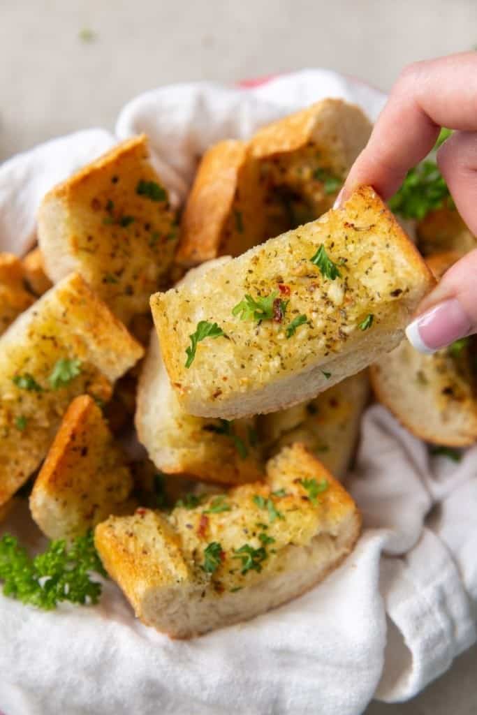 Hand picking up a piece of garlic bread from a basket