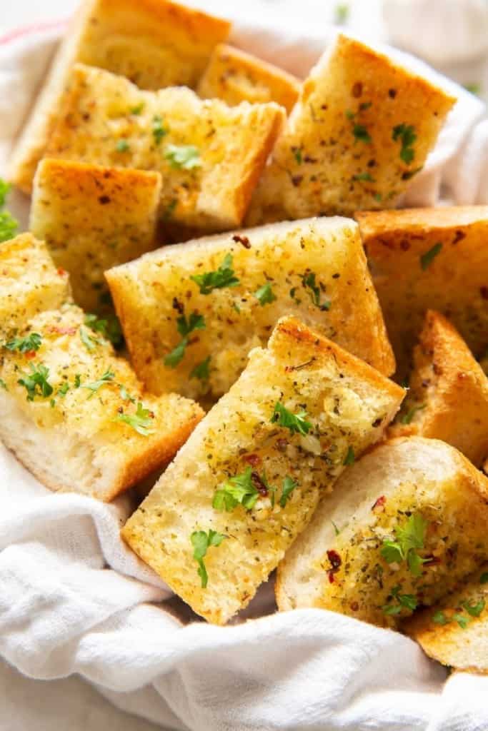 Air Fryer Garlic Bread sliced in a basket with a white cloth underneath with parsley on top