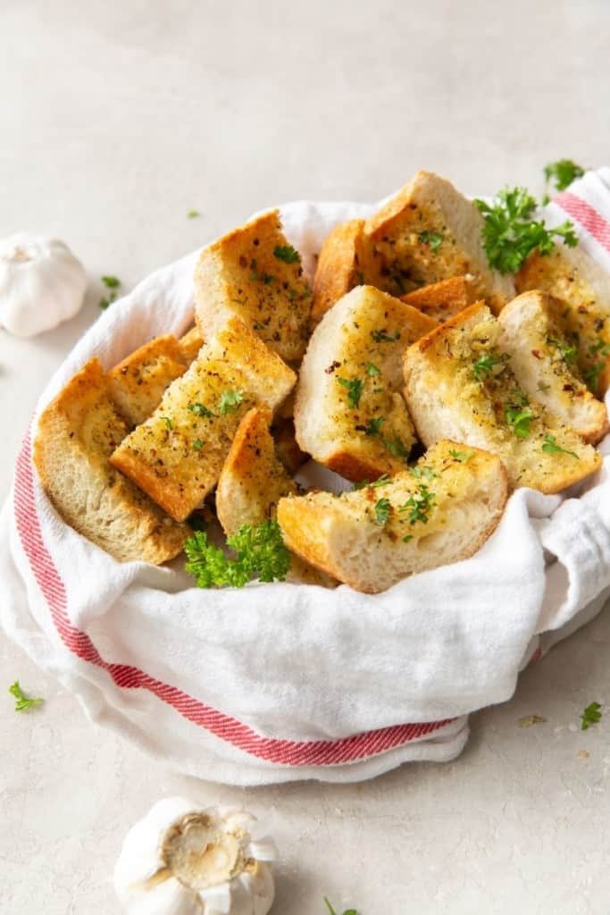 Air Fryer Garlic Bread slices inside a basket with garlic bulbs around it