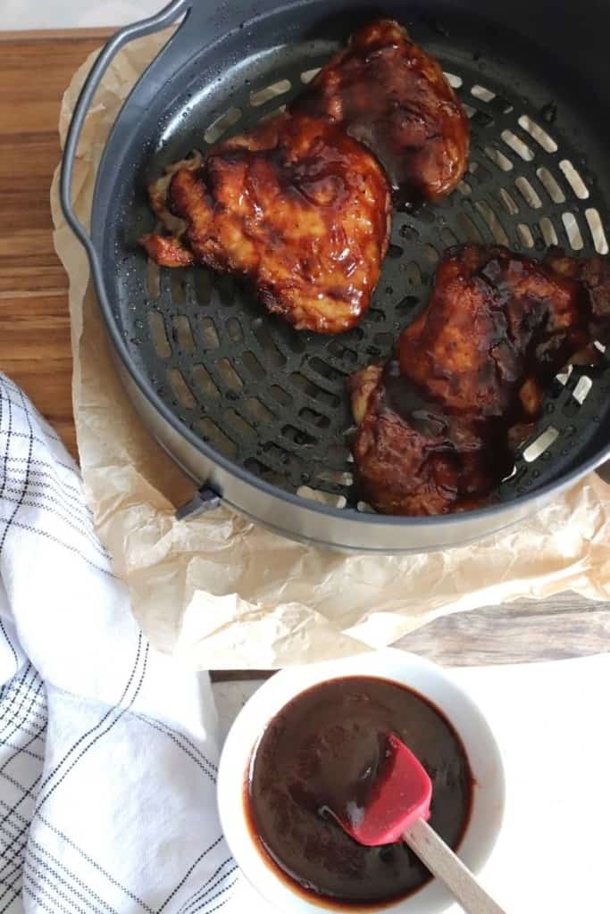 Fully cooked BBQ chicken thighs in Ninja Foodi with a bowl of BBQ sauce and basting brush