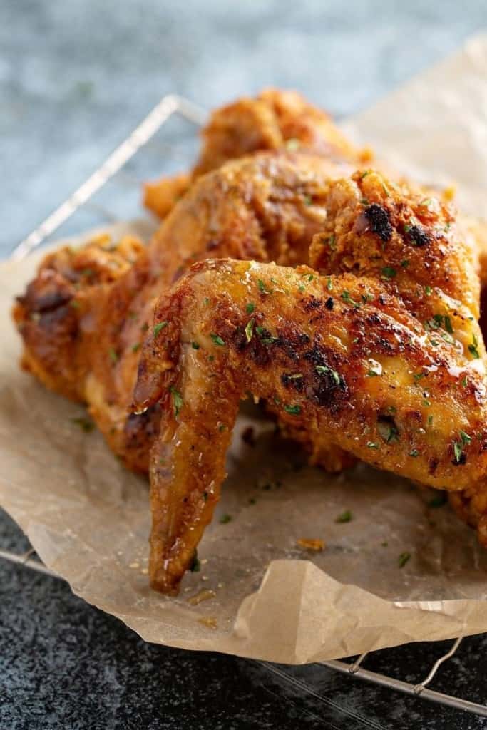 Cooked whole chicken wings on a piece of parchment paper on top of a cooling rack