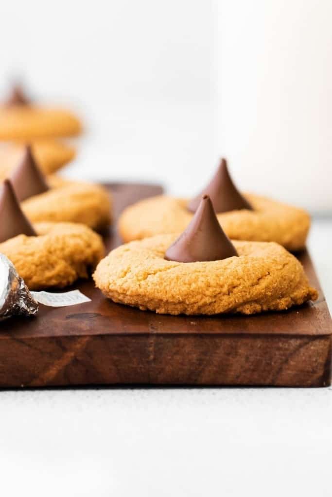 Closeup of peanut butter cookies with hershey kisses in the middle from the side on a brown cutting board