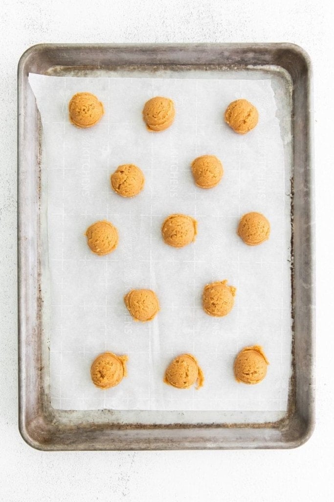 Scoops of cookie dough on a baking sheet with parchment paper