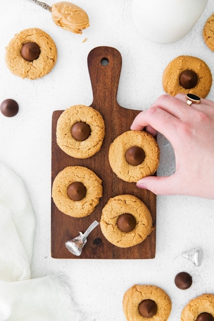 Hand grabbing a peanut butter blossom cookie off a brown cutting board