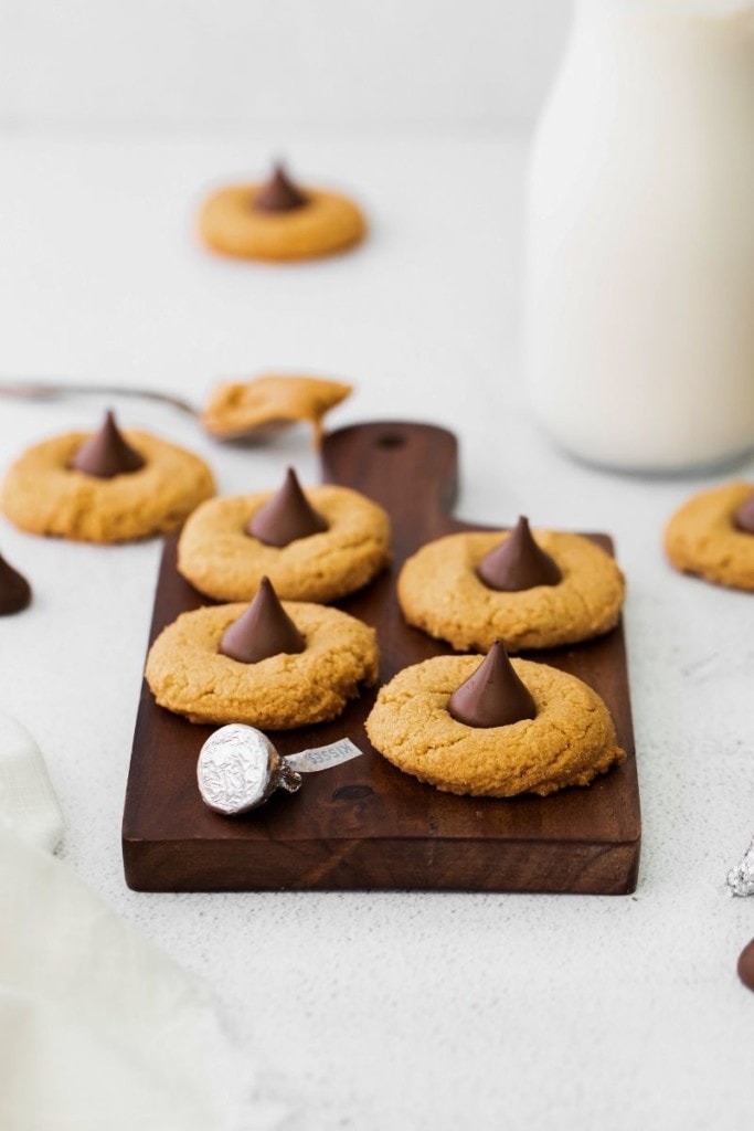Peanut Butter Blossoms on a brown cutting board with a glass of milk in background
