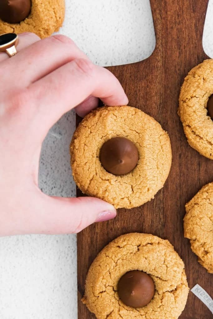 Hand grabbing a cooked peanut butter blossom cookie on a brown cutting board