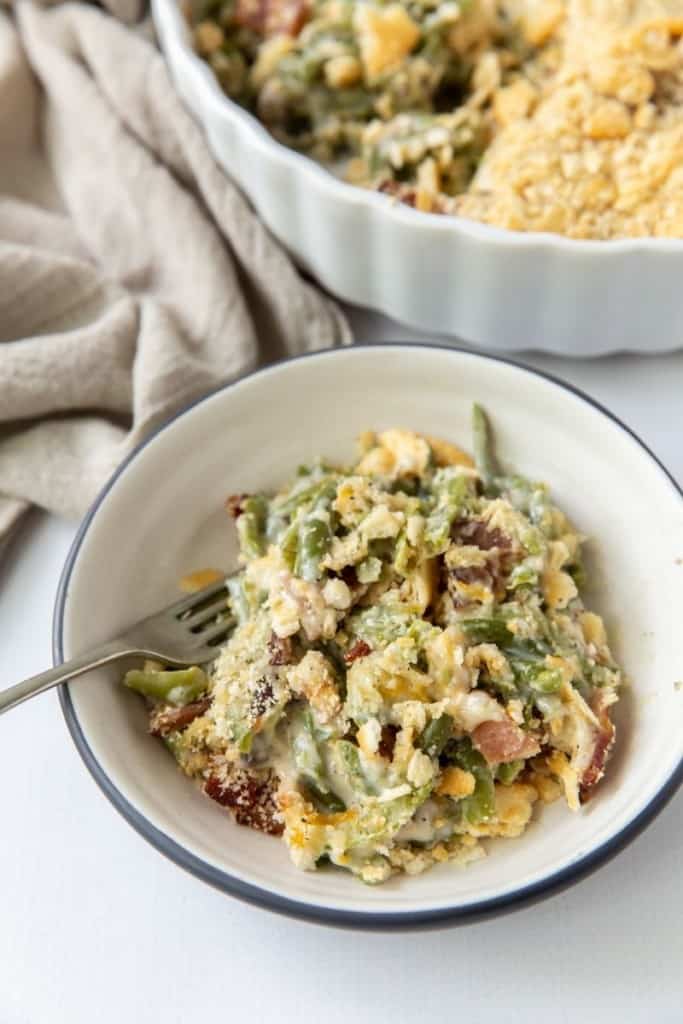 Bowl of ritz cracker green bean casserole with a fork inside and casserole dish in the corner