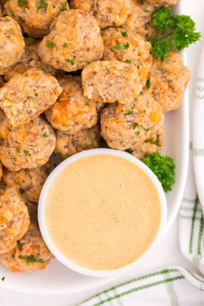 Sausage balls on a serving platter with a small bowl of honey mustard
