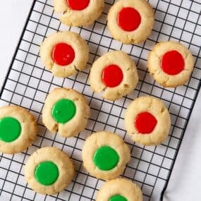 Thumbprint cookies with icing that's red and green on a wire rack.