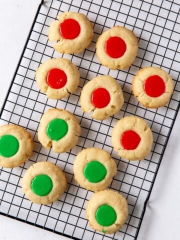 Thumbprint cookies with icing that's red and green on a wire rack.