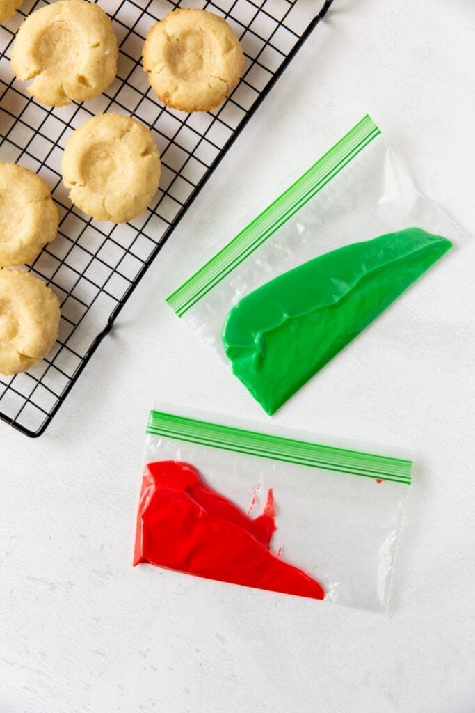 Red and green icing in Ziploc bags ready to ice the thumbprint cookies with frosting.