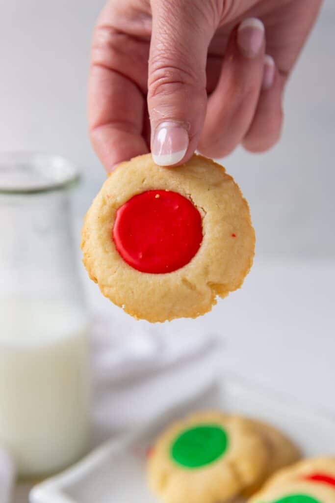 A hand holding a thumbprint cookies recipe with red icing up.