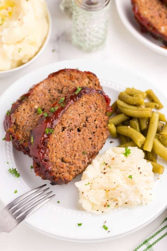 Two meatloaf slices on a plate with mashed potatoes and green beans