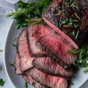 Air Fryer Roast beef cooked to medium rare with pink in the middle with half cut into slices on a serving platter