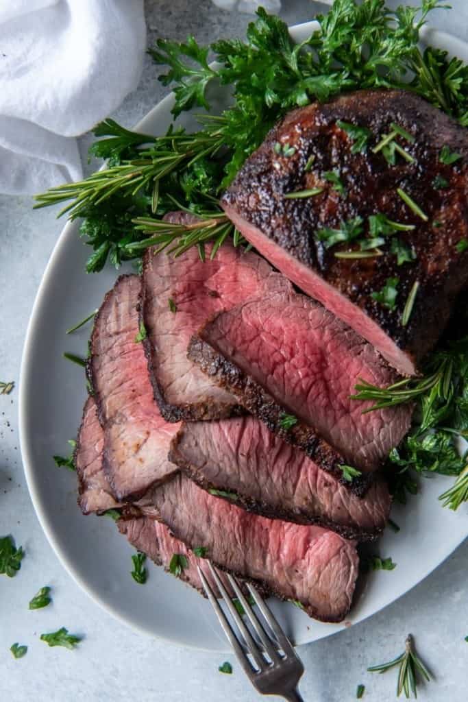 Air Fryer Roast beef cooked to medium rare with pink in the middle with half cut into slices on a serving platter