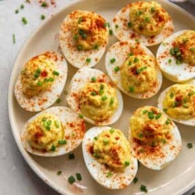 Deviled eggs served on a white round plate and sprinkled with paprika and chives