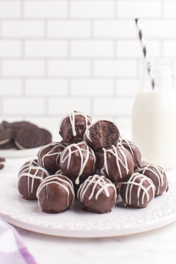 Oreo truffles on a white circular serving plate with a glass on milk in the background 
