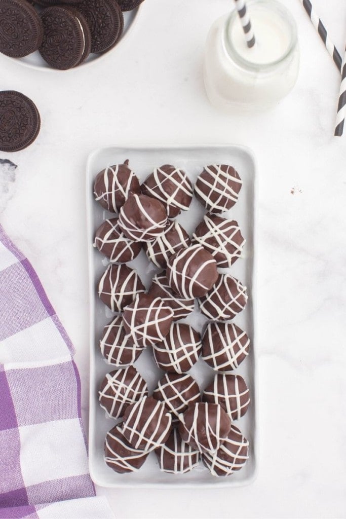 Oreo balls plated on a rectangular serving plate with extra Oreos and milk behind them