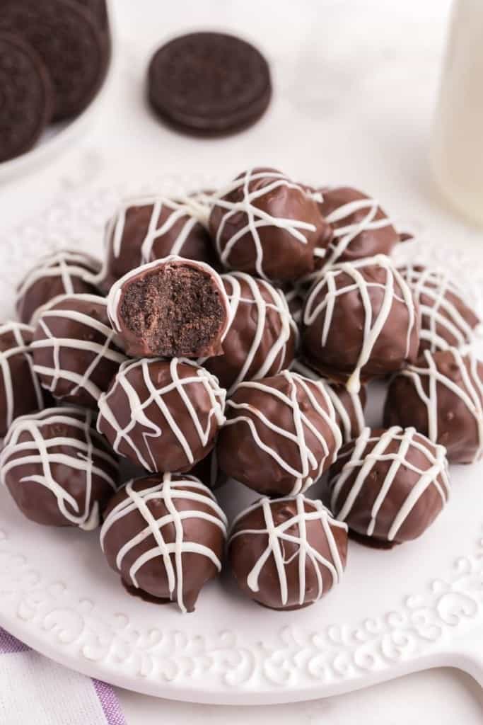 Oreo Balls on a white circular plate drizzled with white chocolate and one bitten into