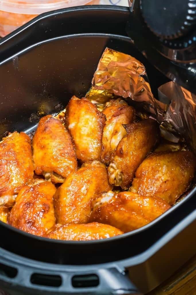 Sauced wings inside air fryer basket with aluminum foil underneath