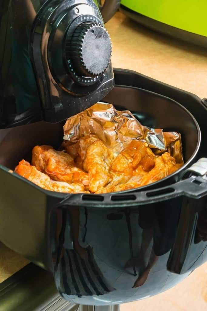 Basket being pulled out of the air fryer with sauced wings inside