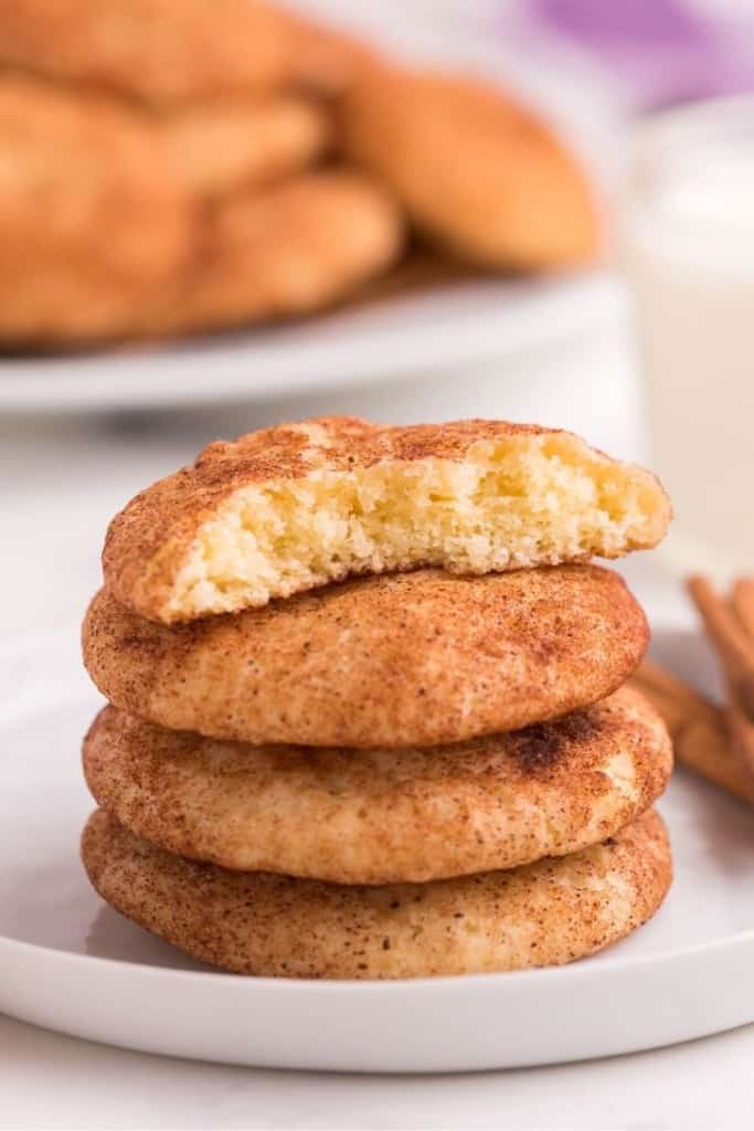 Snickerdoodle cookie with no cream of tartar stacked on top of each other on a white plate with top cookie broken in half