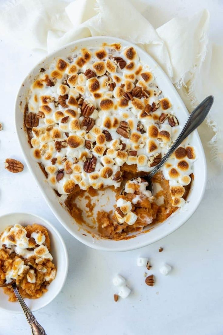 Finished sweet potato casserole with roasted marshmallows and pecans and a serving spoon inside