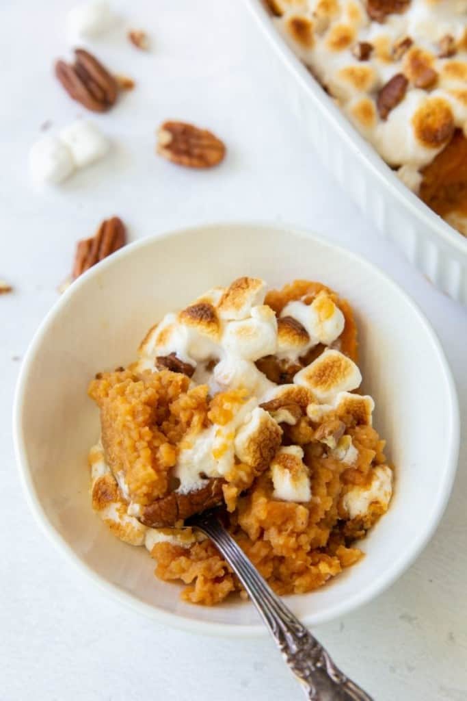 Scoop of sweet potato casserole in a white bowl with a spoon