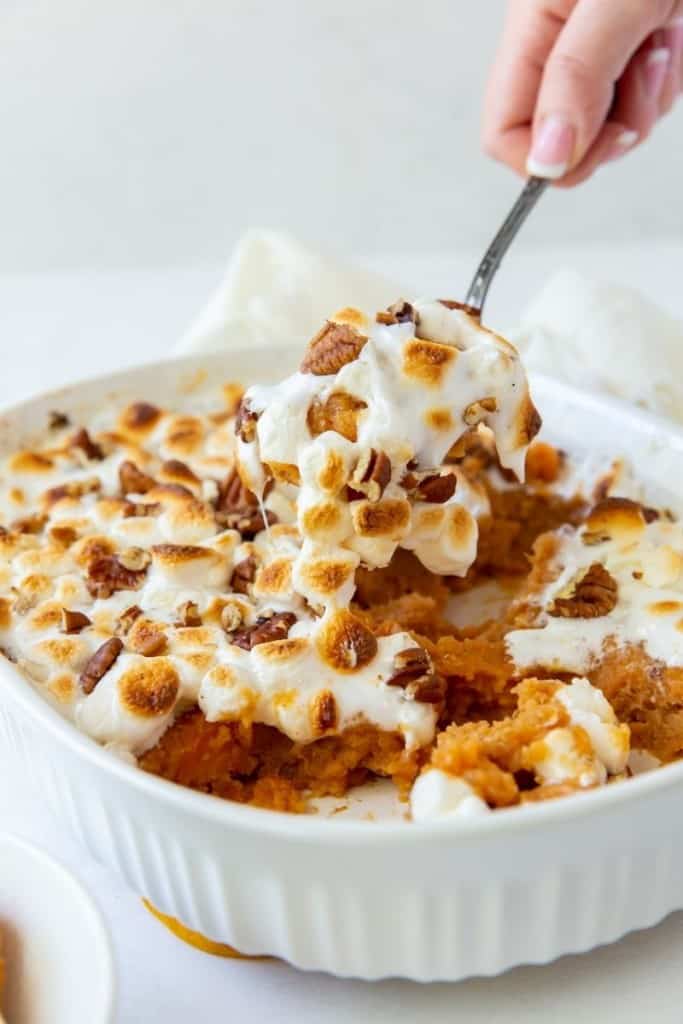 Sweet Potato Casserole with a hand pulling a serving spoon piece out
