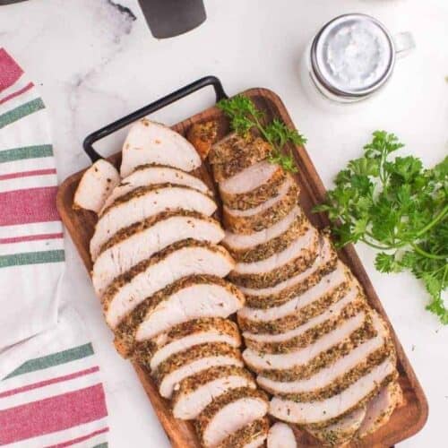 Air Fryer Turkey Tenderloins sliced up on a wooden serving platter in front of an air fryer