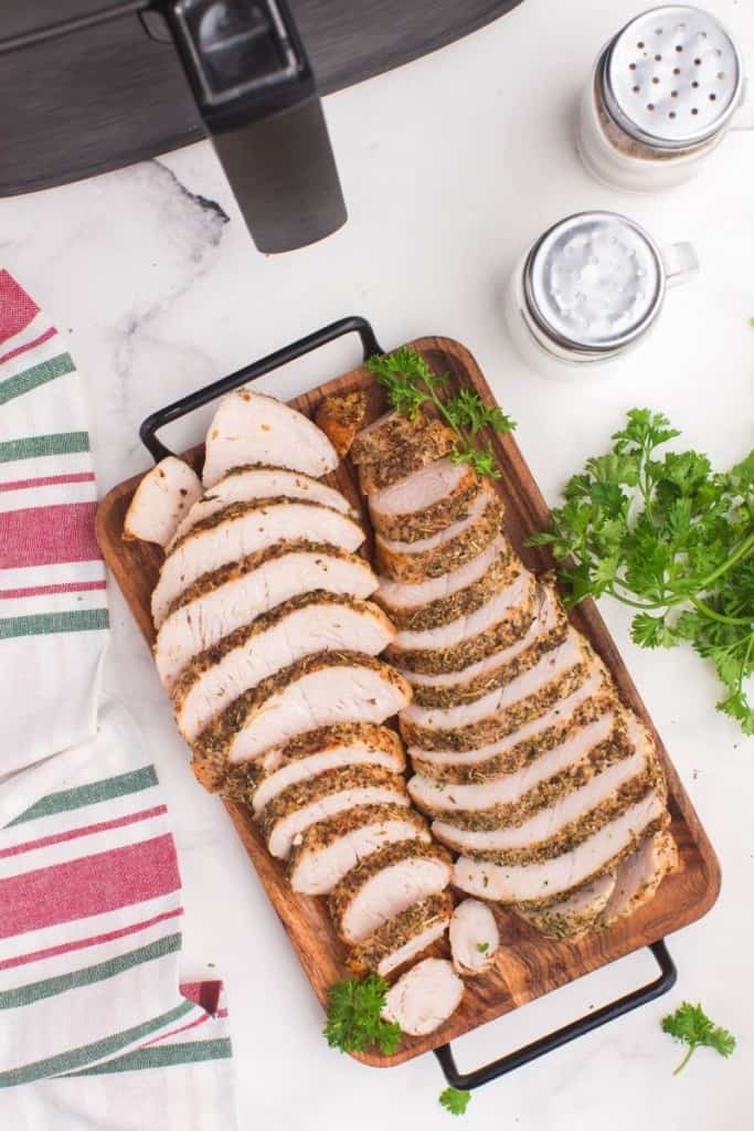 Air Fryer Turkey Tenderloins sliced up on a wooden serving platter in front of an air fryer