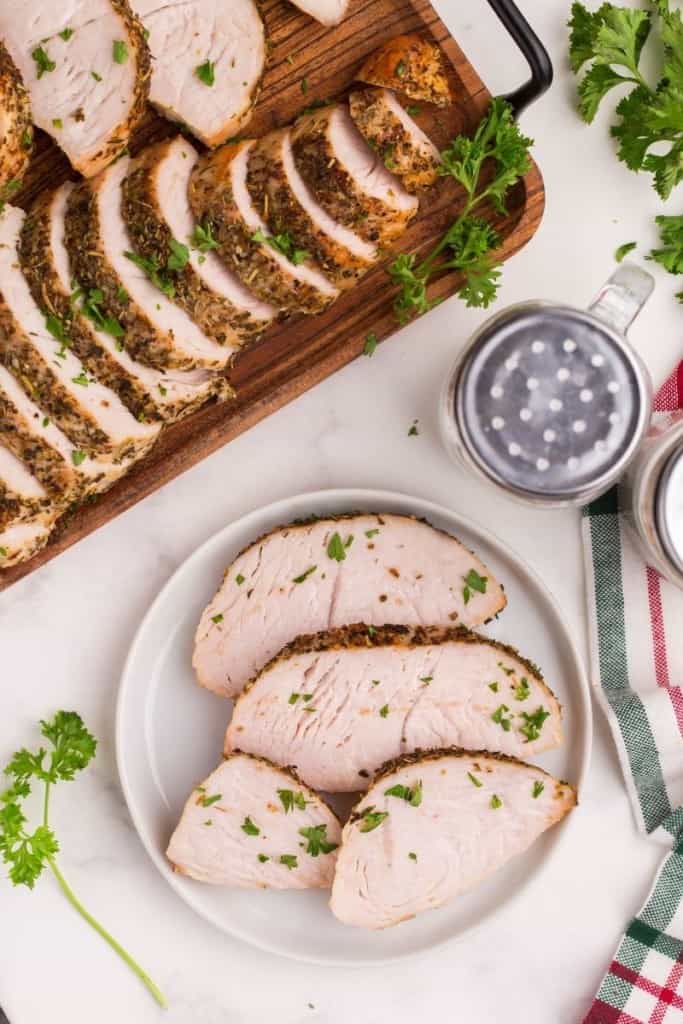 Turkey Tenderloin served on a round white plate with remaining sliced turkey on a wooden serving tray in back