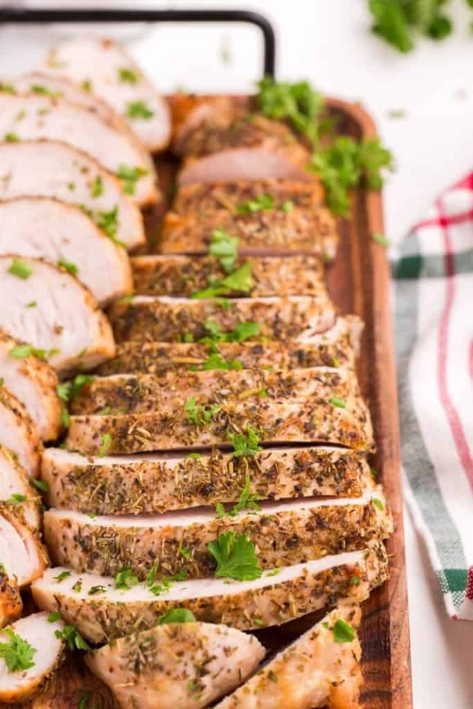 Closeup of sliced turkey tenderloins on a wooden serving tray with outside of tenderloins showing