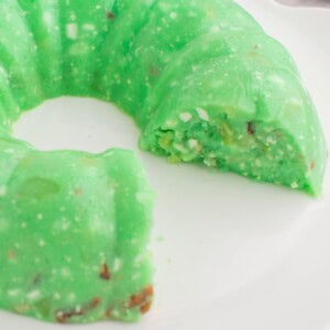 Lime jello salad with cottage cheese on a serving plate with a few pieces missing.