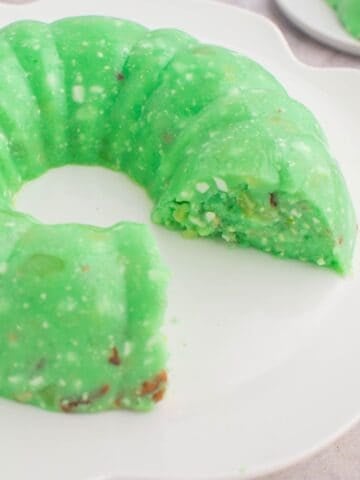 Lime jello salad with cottage cheese on a serving plate with a few pieces missing.