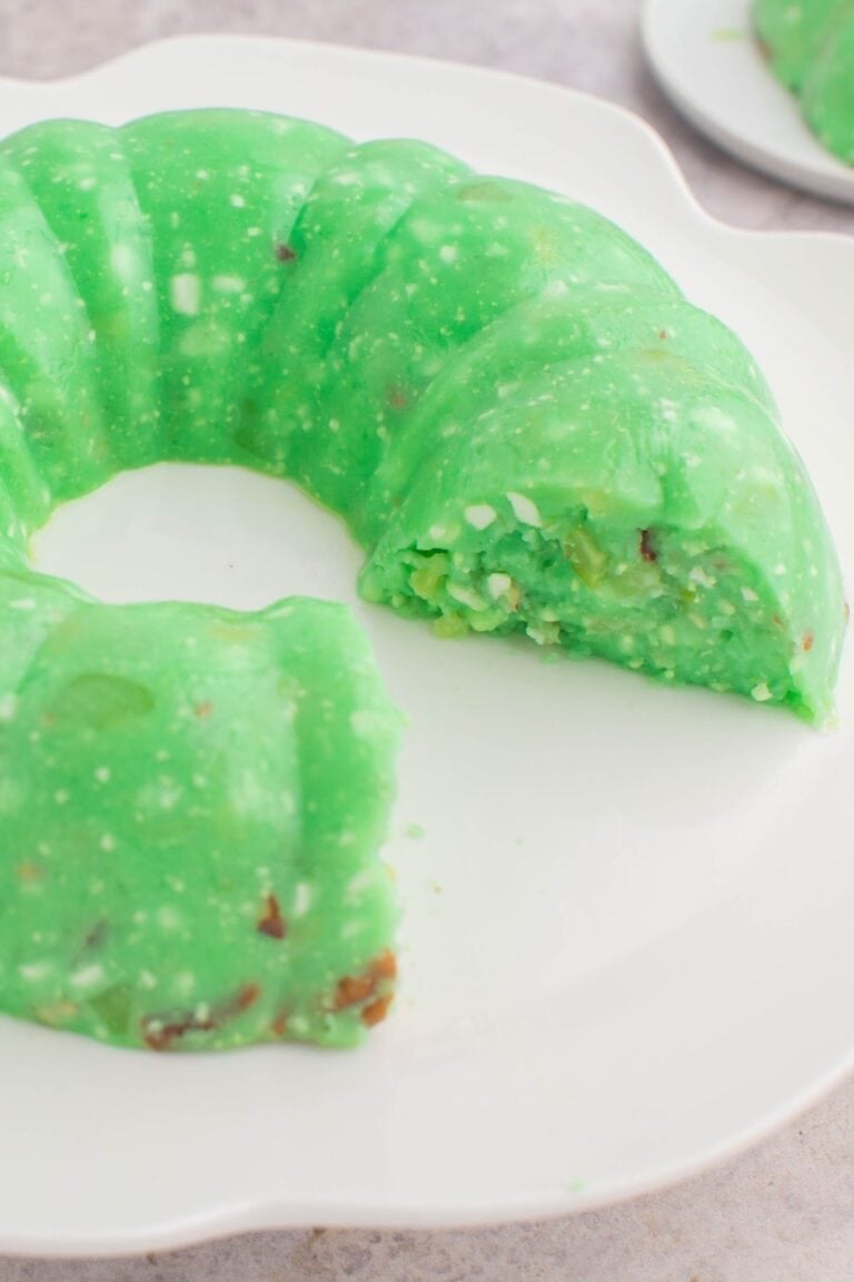 Lime jello salad with cottage cheese on a serving plate with a few pieces missing.